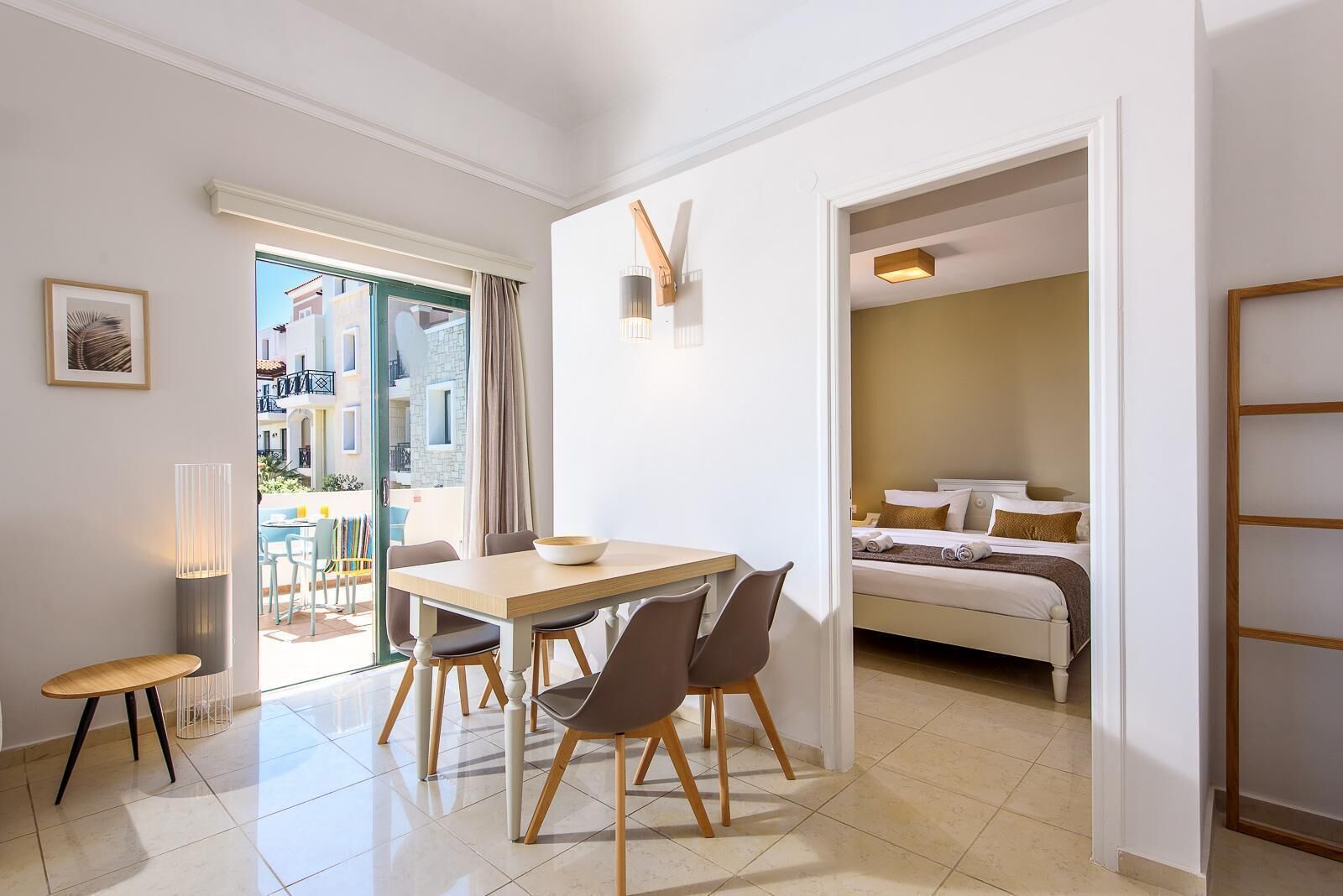 Quarto de hotel moderno com área de refeições, cama com vista e varanda com mobiliário para área externa.