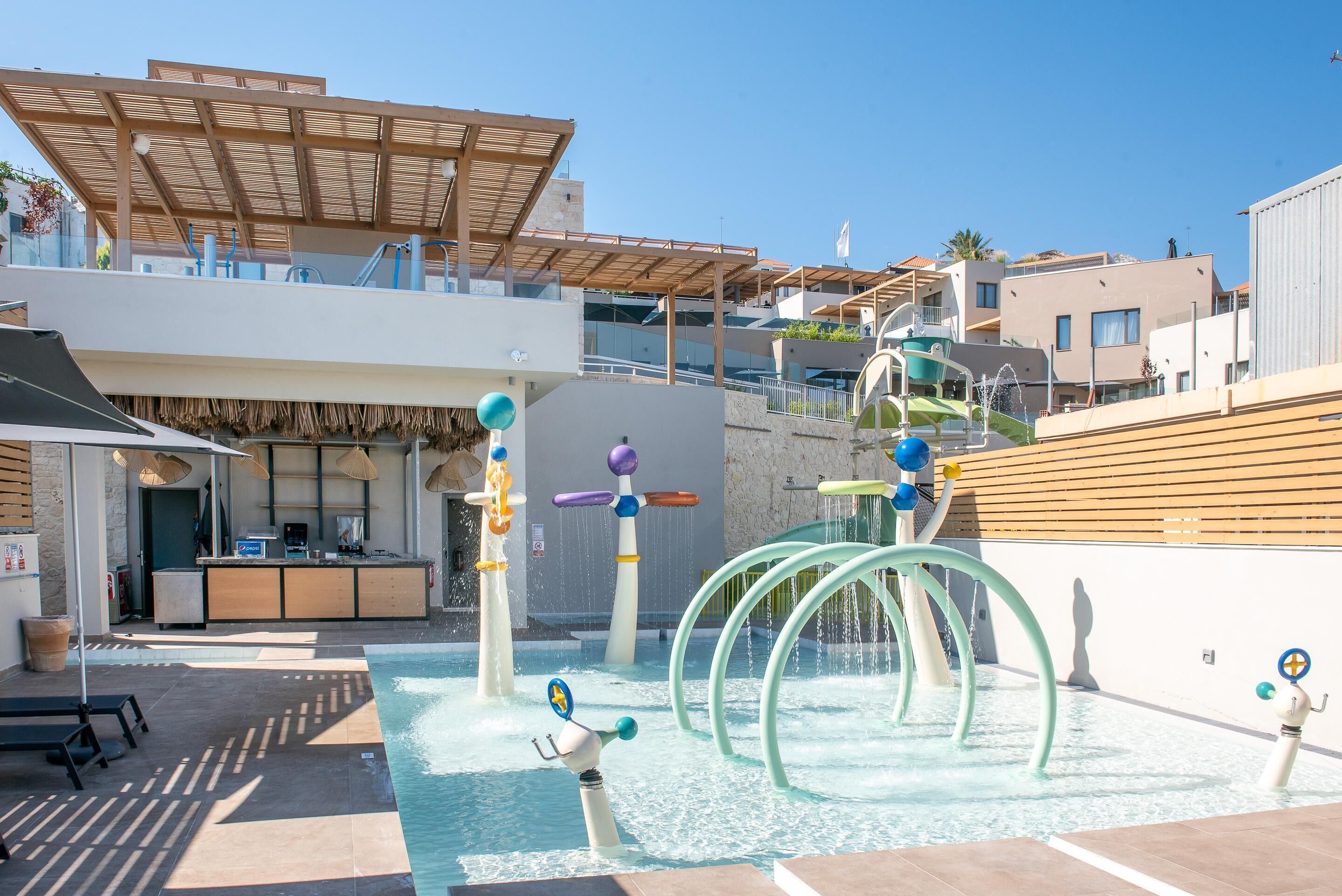 A rooftop pool area with water play structures, a bar, and outdoor seating.