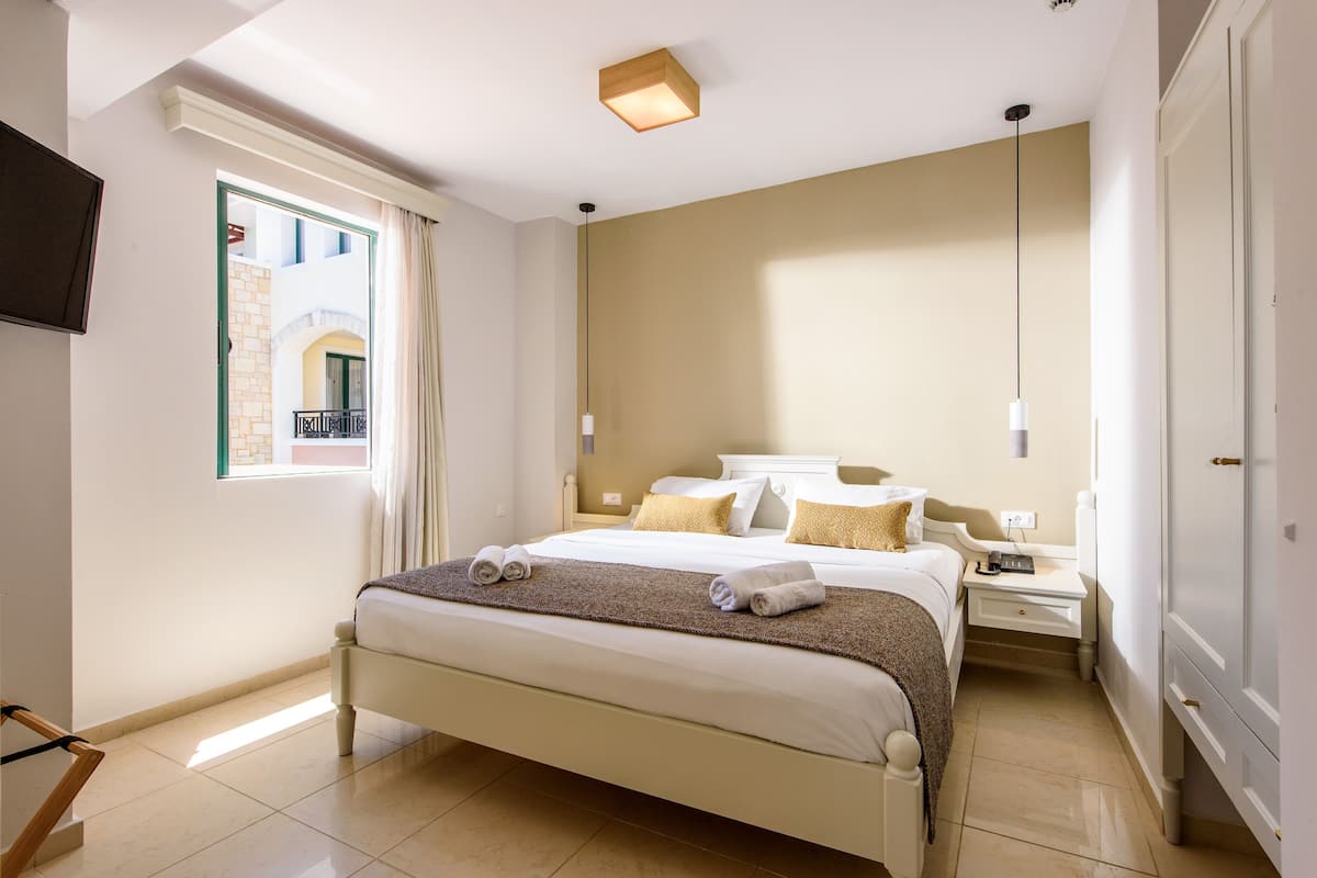 A hotel room with a large bed, a bedside table, a wardrobe, a TV mounted on the wall, and a window with curtains.