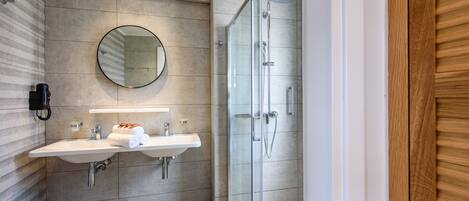 A modern bathroom with a large mirror, two sinks, and a glass-enclosed shower.