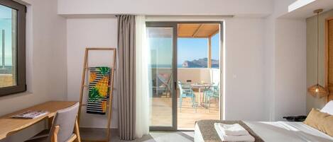 Habitación de hotel con cama, escritorio, silla, balcón con mesa y sillas, y vista al mar.
