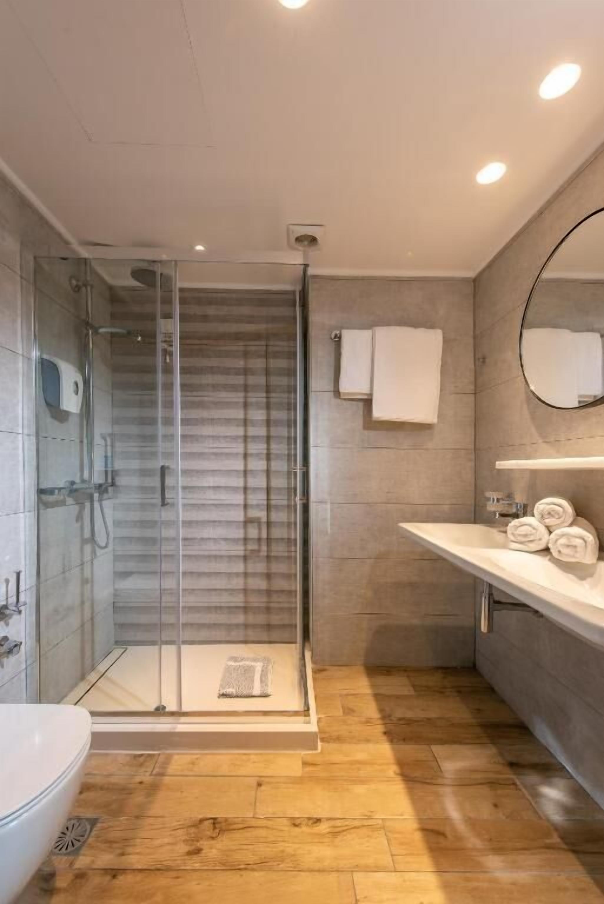Une salle de bain moderne avec une douche à parois de verre, un lavabo blanc avec un miroir et un plancher en bois.