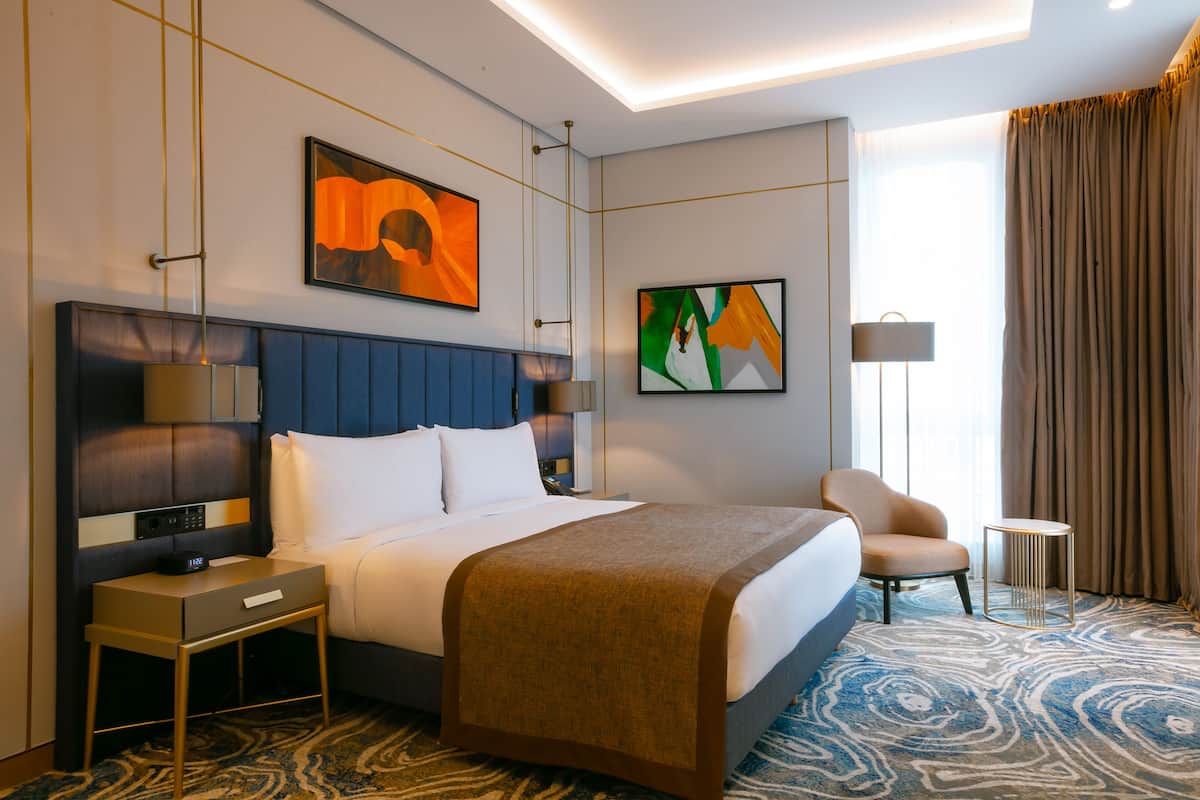 Camera d'albergo con un letto grande, un comodino, una sedia e due lampade a parete.