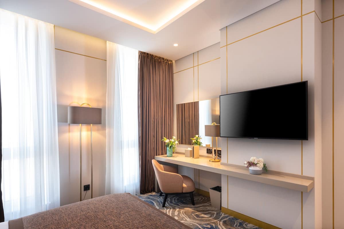 Una moderna camera d'albergo con un letto grande, una scrivania con una sedia, una TV a schermo piatto e un'ampia finestra con tende.