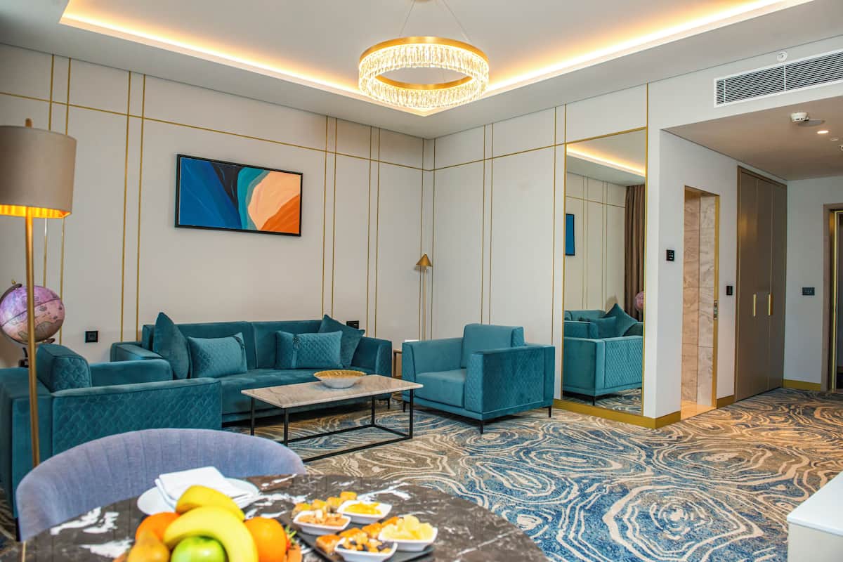 Una moderna camera d'hotel con divani color petrolio, un tavolino da caffè in marmo con della frutta, un grande quadro astratto e una moquette fantasia.