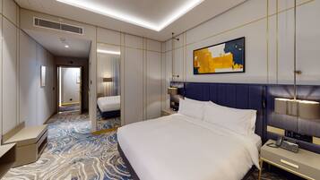 A hotel room with a large bed, bedside tables, a mirror, a painting, and a carpeted floor.