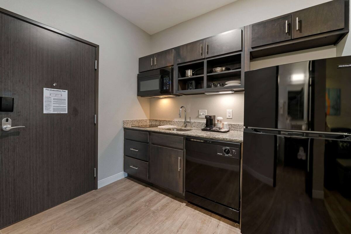 A modern kitchen with dark wood cabinets, a stainless steel refrigerator, a microwave, and a dishwasher.