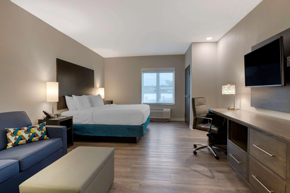 A hotel room with a bed, a desk, a chair, a couch, and a TV.