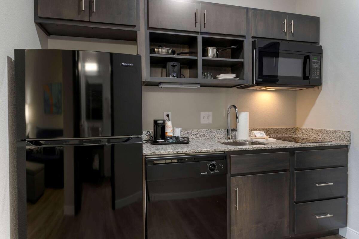 A modern kitchen with dark cabinetry, a built-in microwave, a coffee maker, and a dishwasher.