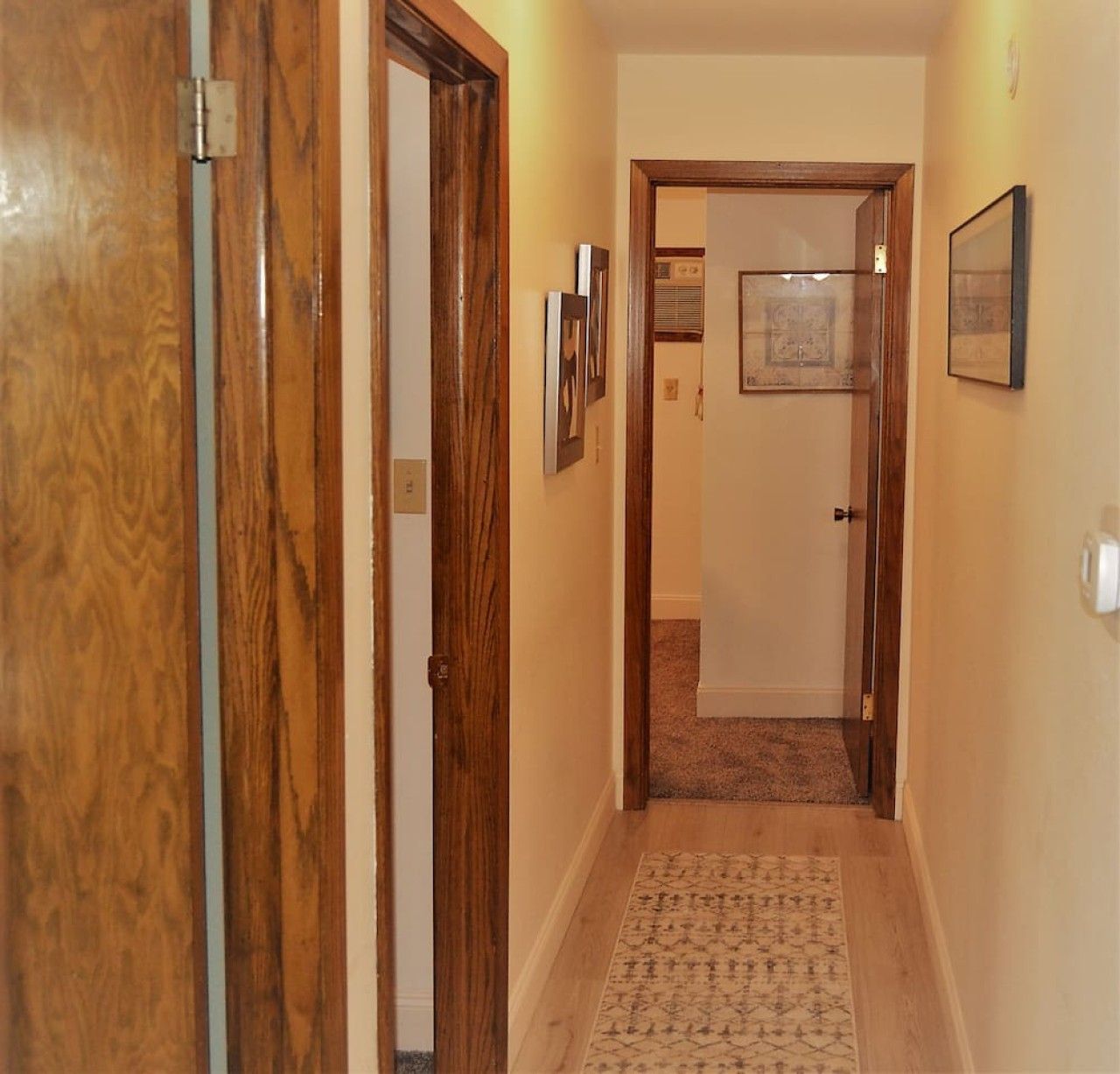 A hallway with wooden doors, a carpeted floor, and framed pictures on the wall.