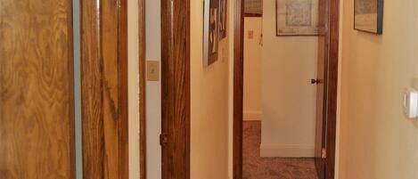 A hallway with wooden doors, a carpeted floor, and framed pictures on the wall.