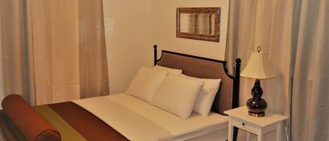 A single bed with a headboard, a bedside table with a lamp, and a mirror on the wall.
