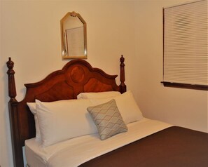 A bed with a wooden headboard, white bedding, and a single patterned pillow.