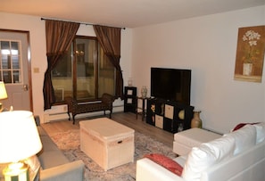 Sala de estar com sofá, banquinho e televisão.