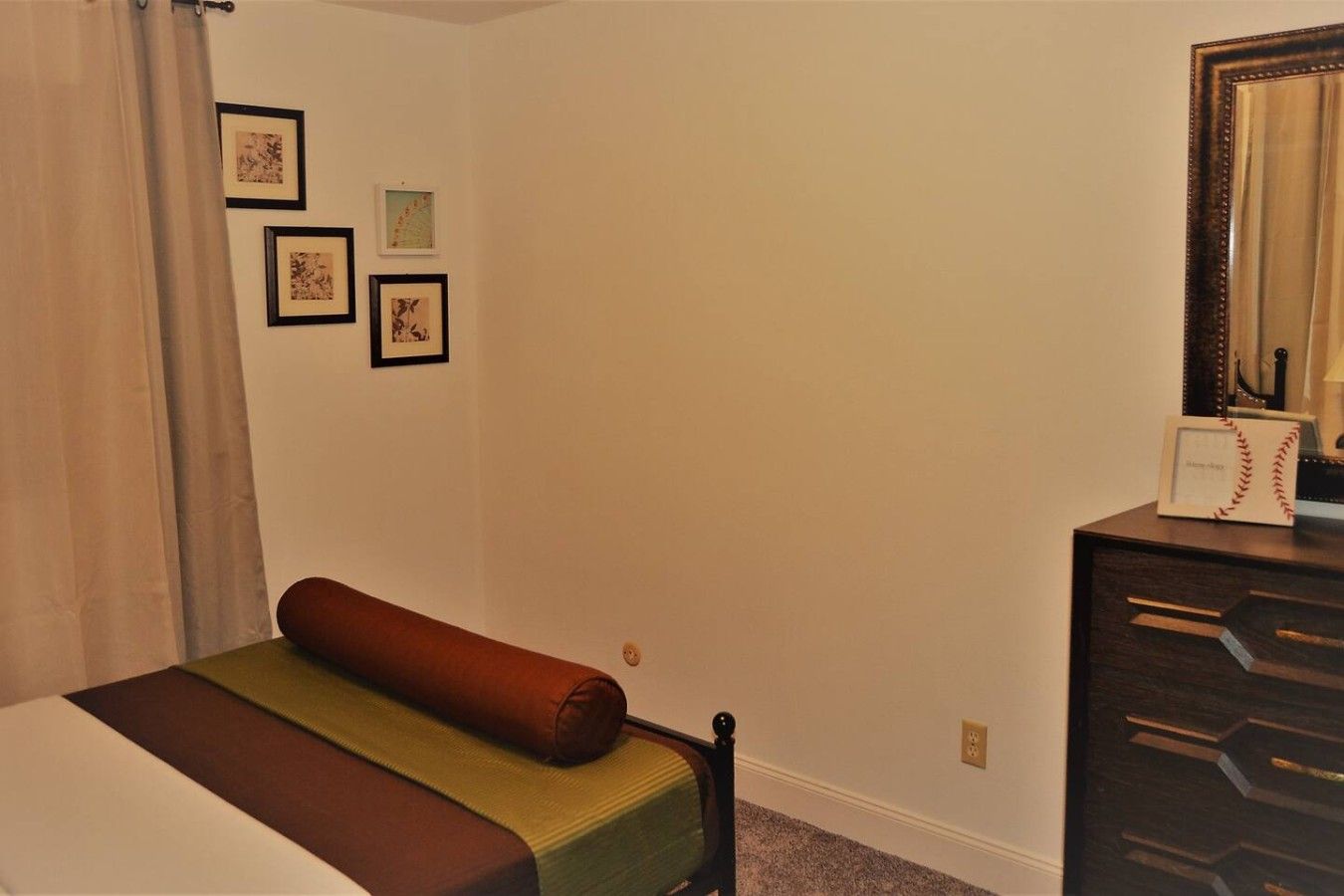 A bedroom with a bed, a dresser, a mirror, and framed pictures on the wall.