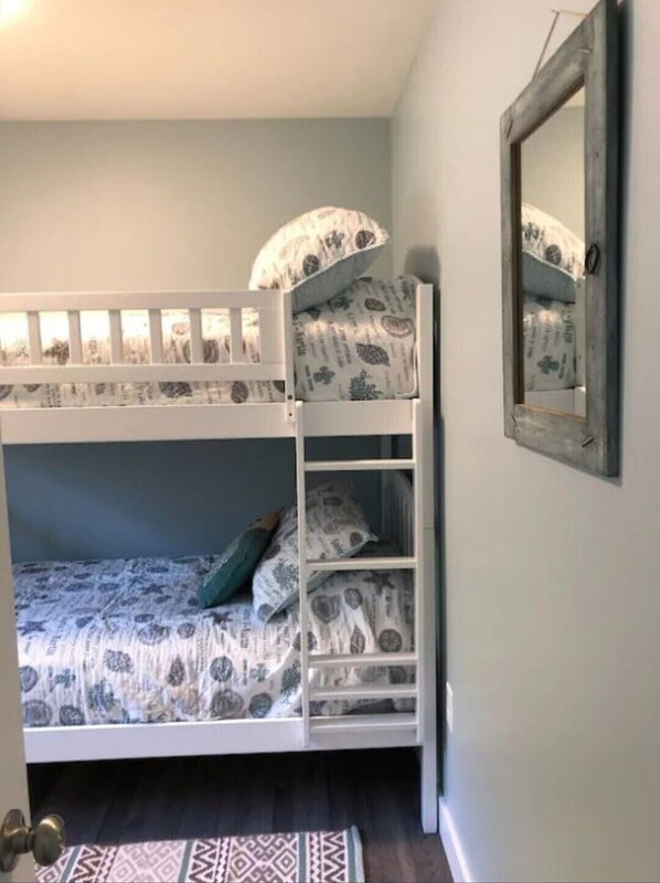 Una cama litera con ropa de cama estampada, un pequeño estante y un espejo en la pared.