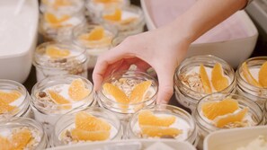 En hånd vælger et glas yoghurt med appelsinskiver.