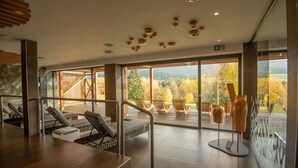 Un espacio interior moderno con una escalera de madera, sillones de descanso y vistas a árboles otoñales a través de amplios ventanales.