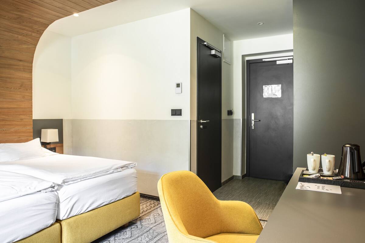 A hotel room with a bed, a desk with a coffee maker, and a door.