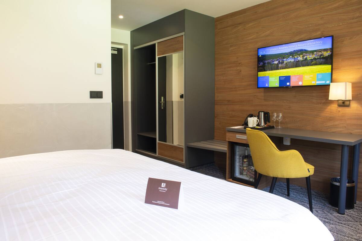 A hotel room with a bed, a desk, a TV, and a yellow chair.