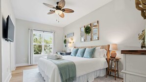 A bedroom with a bed, a ceiling fan, a TV, and a window with a view of trees. - Wanderlust- Dog Friendly- Renovated 2026 (Santa Rosa Beach)