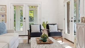 A spacious living room with a light-colored sofa, a dark sofa with patterned cushions, a wooden coffee table with decorative items, and a large window with a view of greenery. - Wanderlust- Dog Friendly- Renovated 2026 (Santa Rosa Beach)