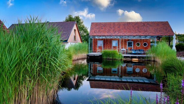 A house with a red roof, a wooden deck, and a pond in front.