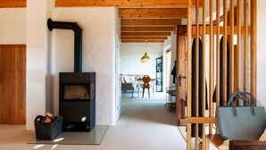 A modern living room with a wood-burning stove, a dining area, and a hallway leading to a bedroom.