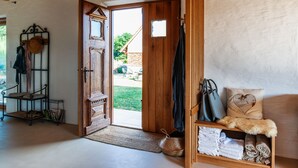 A room with a wooden door leading outside, a bench with towels, a hat rack, and a shelf with bags and a heart-shaped pillow.