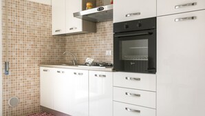A modern kitchen with white cabinets, a stainless steel range hood, and a black oven. - Chic Aprtment 10 min to Venice (Mestre)