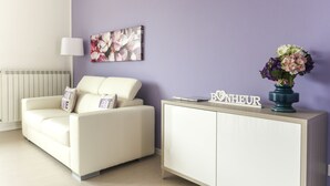 A living room with a white sofa, a cabinet, a floral painting, and a vase with flowers. - Chic Aprtment 10 min to Venice (Mestre)