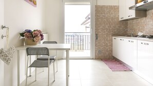 A modern kitchen with white cabinets, a dining area with a table and chairs, and a balcony with a view. - Chic Aprtment 10 min to Venice (Mestre)