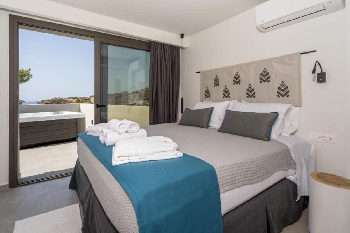 A modern hotel room with a large bed, a balcony with a view, and a small side table.