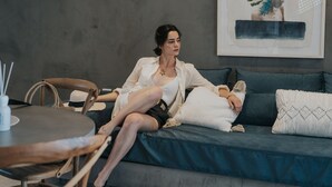 A person sitting on a dark blue couch with a white pillow and a decorative pillow. There is a table with a white candle and a vase with a plant. A framed artwork is on the wall. - Pignolia Suites - Adults Only (Ierapetra)