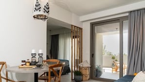 A modern living room with a round dining table, wooden chairs, a sofa, and a balcony with a view. - Pignolia Suites - Adults Only (Ierapetra)