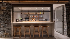 A kitchen with a bar area, wooden stools, and a stone wall. - Pignolia Suites - Adults Only (Ierapetra)