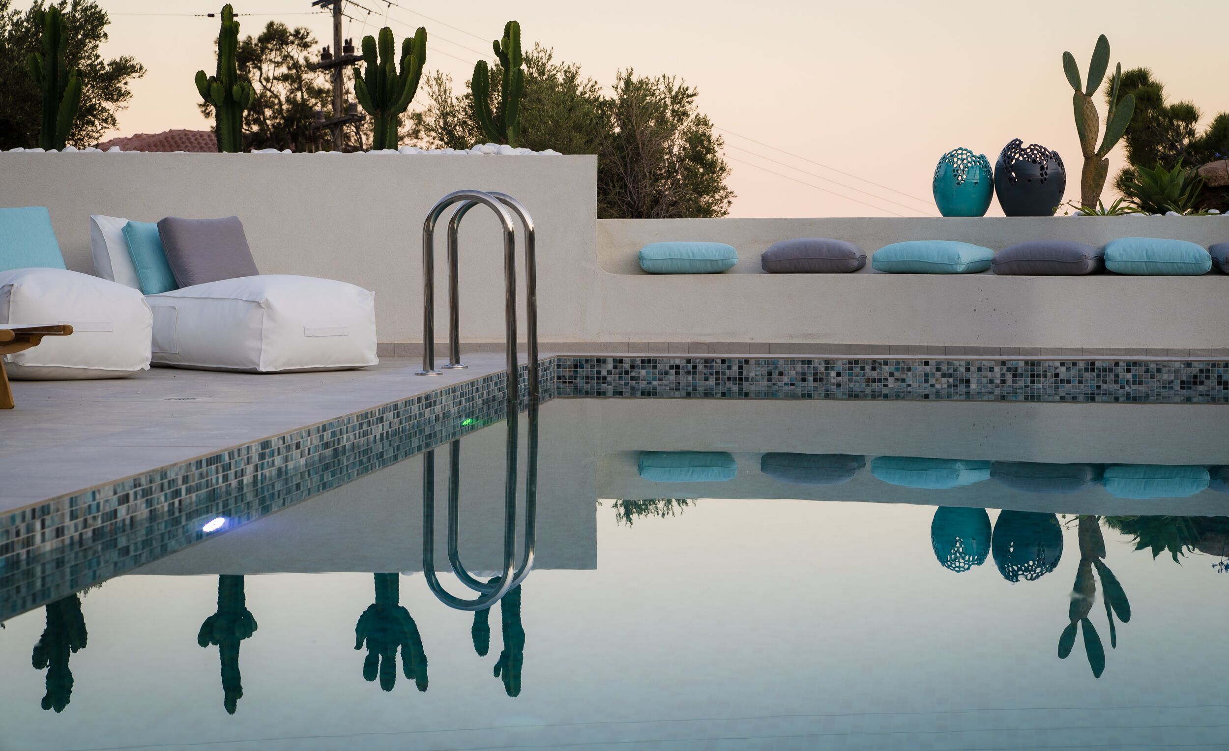 A pool area with a white sofa and cushions, a metal ladder, and cacti in the background.