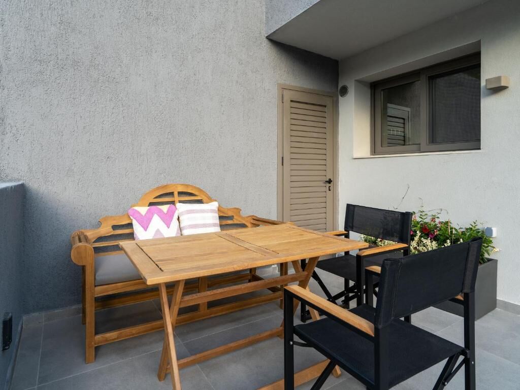 Une table et des chaises en bois sont placées contre un mur gris, près d’une fenêtre et d’une porte.