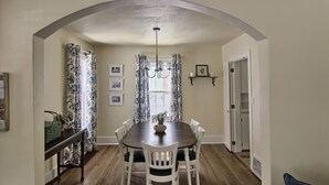 Un comedor con una mesa de madera oscura, sillas blancas y cortinas estampadas.