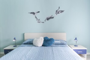 Een slaapkamer met een bed, twee nachtkastjes, wanddecoratie van vogels en een blauw-wit kleurenschema.