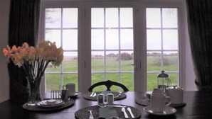 A dining table set for four with a view of a grassy field through large windows. - Wagtail Lodge Boutique Country House B&B, Stonehaven (Stonehaven)