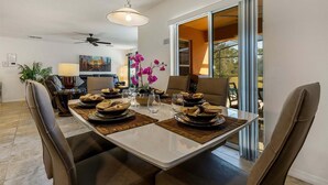A dining area with a table set for four, chairs, a ceiling fan, and a view through a glass door.