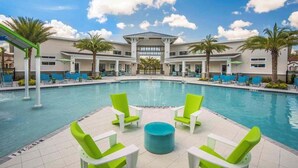 A pool area with lounge chairs, a central table, and a building with a flat roof and large windows.