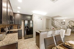 A modern kitchen with dark wood cabinets, a stainless steel refrigerator, and a granite countertop.