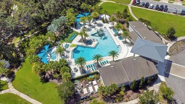 An aerial view of a resort with multiple swimming pools, palm trees, and a parking lot.