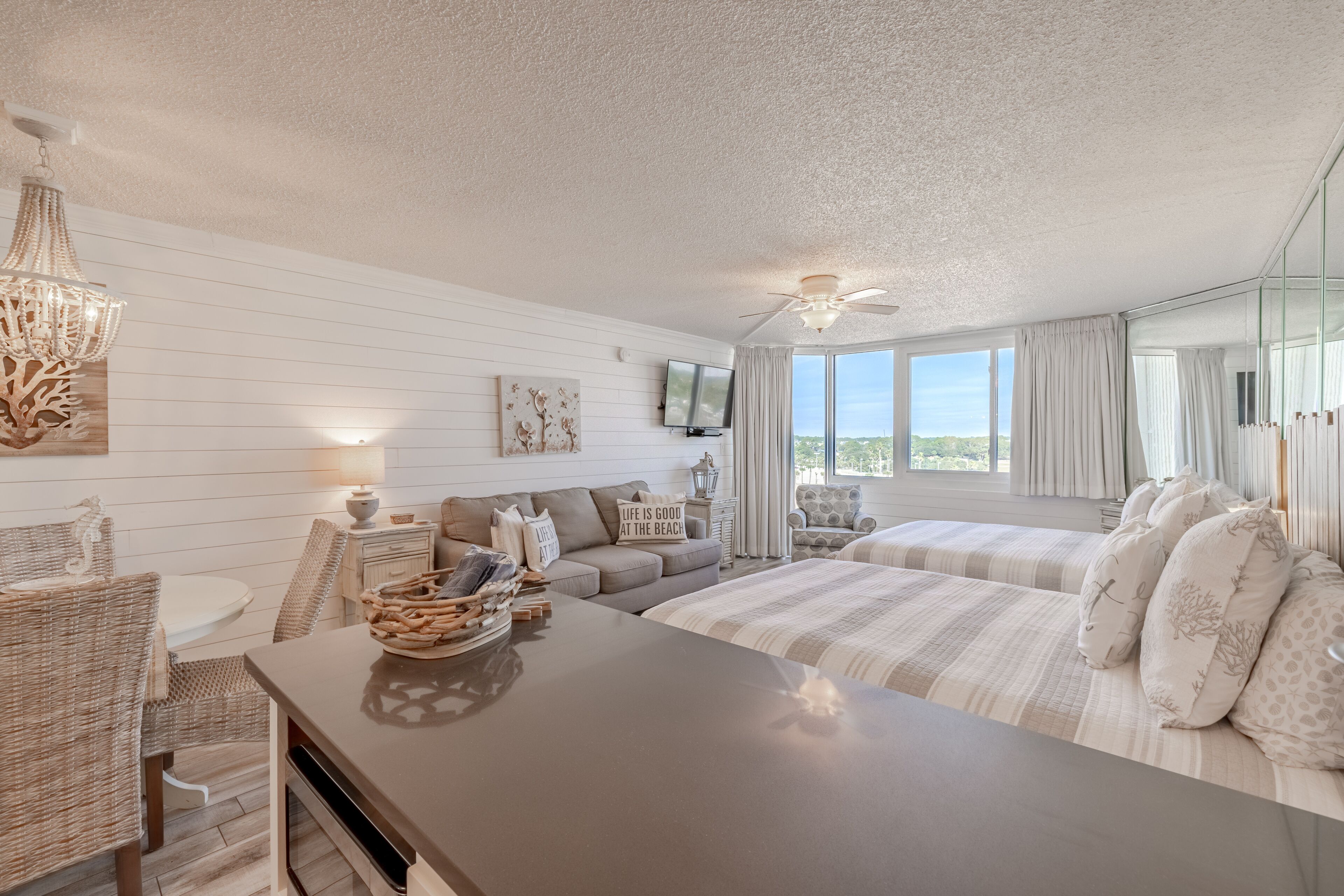 A bedroom with a bed, a desk, a television, and a view of the outdoors.