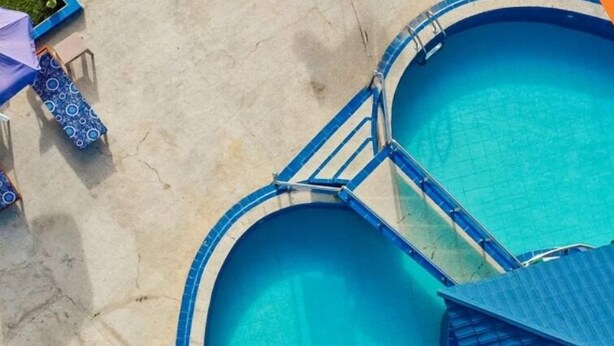An aerial view of a swimming pool with two separate sections connected by a bridge, surrounded by a sandy area with lounge chairs and umbrellas. - Amazing Seaview Room | Cape Point, Bakau (Bakau)