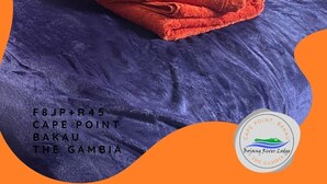 A bed with a folded red towel and a pillow. Text indicates location and lodge name. - Amazing Seaview Room | Cape Point, Bakau (Bakau)