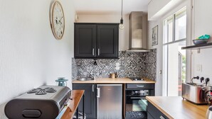 A compact kitchen with dark cabinets, a patterned backsplash, a gas stove, a dishwasher, and a small oven. - L'Astrolabe - One Bedroom Apartment, Sleeps 4 (Dinard)