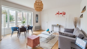 A modern living room with a dining area, a grey sofa, a coffee table, and a hanging woven light fixture. - L'Astrolabe - One Bedroom Apartment, Sleeps 4 (Dinard)